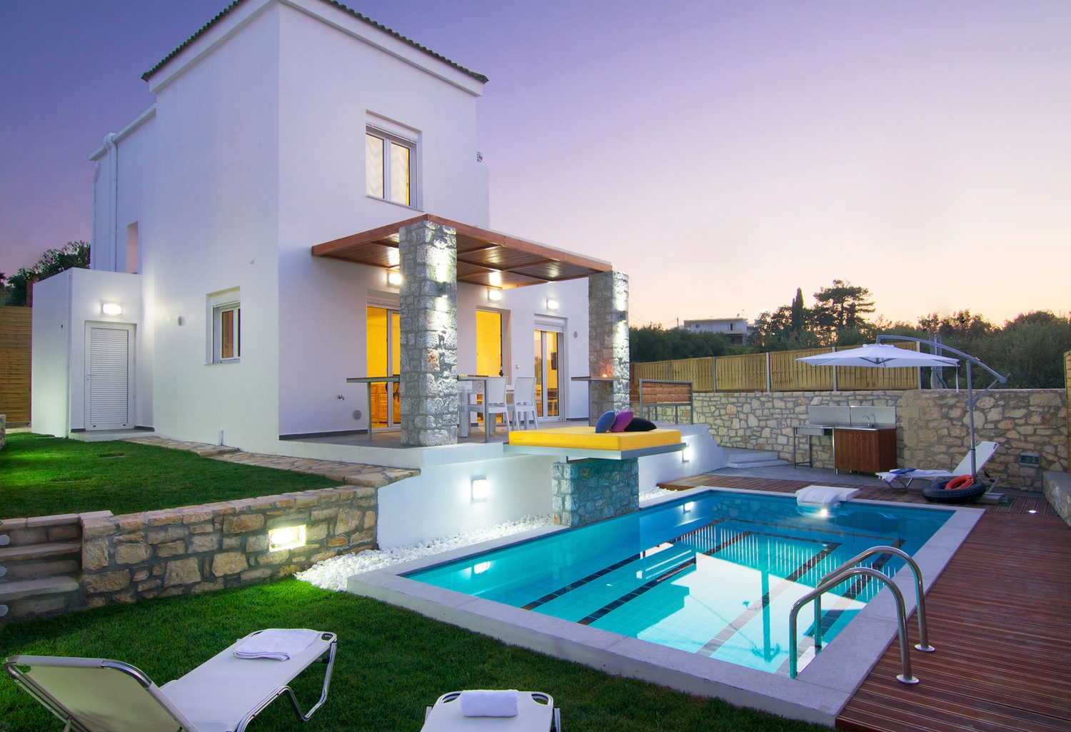 Villa Aada am Abend: beleuchtetes Haus mit türkis leuchtendem Pool und Rasenfläche