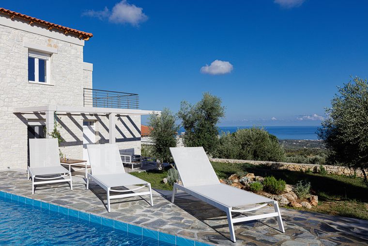 Pool der Villa Eos mit Sonnenliegen, im Hintergrund die Ägäis